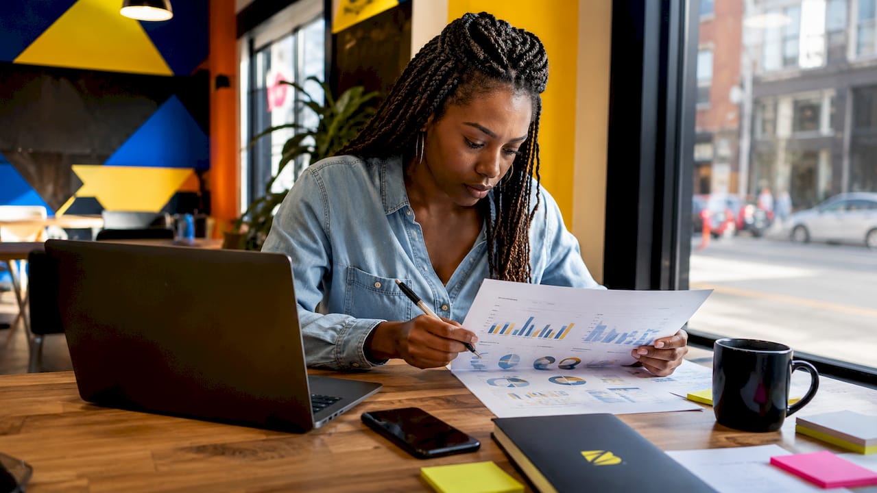Une femme examine attentivement un rapport papier présentant les indicateurs clés de performance de sa stratégie marketing.