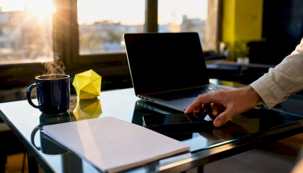 Une main ajuste un smartphone posé sur le bureau, mis en valeur par des éléments de branding.