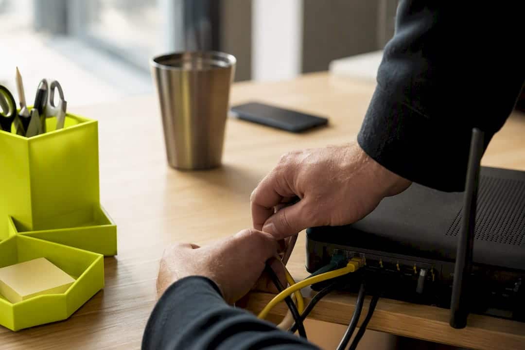 Des mains qui raccordent des câbles réseau sur un bureau.