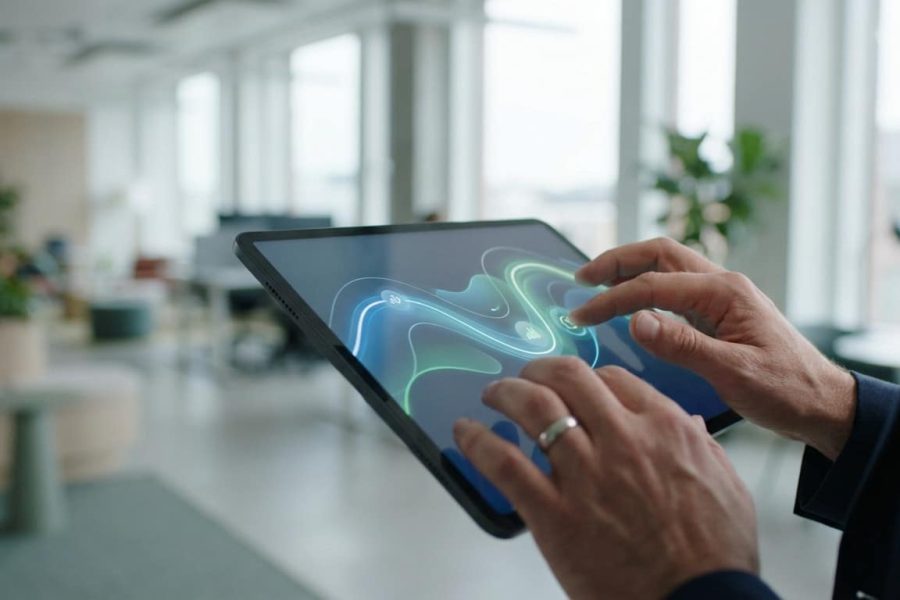 Mains interagissant avec une tablette affichant un design lumineux bleu-vert, symbolisant la conversion ou la performance dans un bureau moderne.